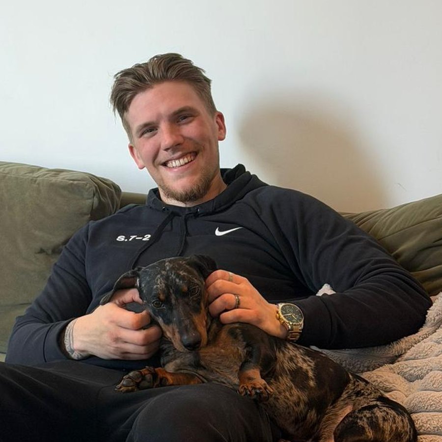 Rob McLellan smiling, sitting on a sofa with his dachshund